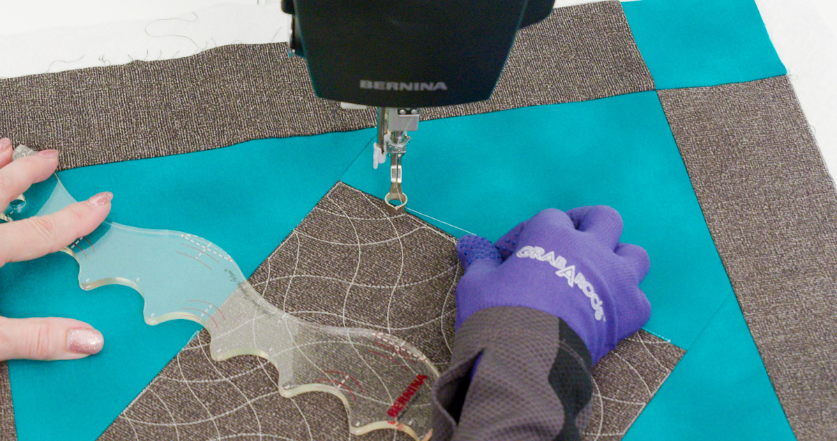 Close-up photo of purple-gloved hands quilting curvy lines on teal and gray fabric with a BERNINA Ruler.