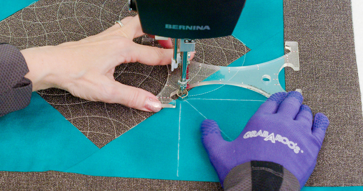 Close-up photo of purple-gloved hands quilting curvy lines on teal and gray fabric with a BERNINA Ruler.