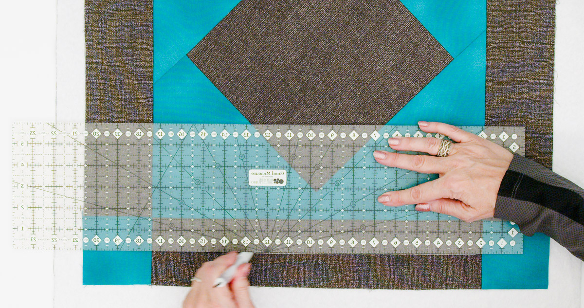 Overhead view of a quilter marking a straight line down the center of a border on the Curvy Quilting Table Topper.