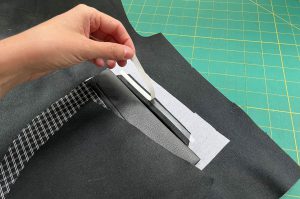 A person is pulling off the protective paper to expose the sticky tape on the top edge of the pocket opening on the wrong side of the project.