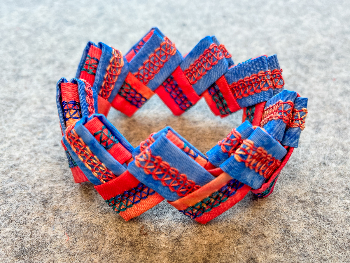 finished serger cuff bracelet in orange and blue fabric on a gray background