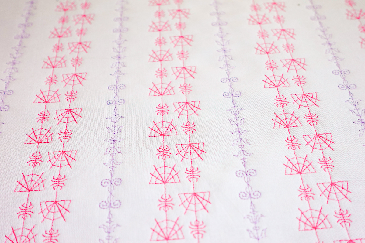 Embroidered spider webs in pink on white fabric