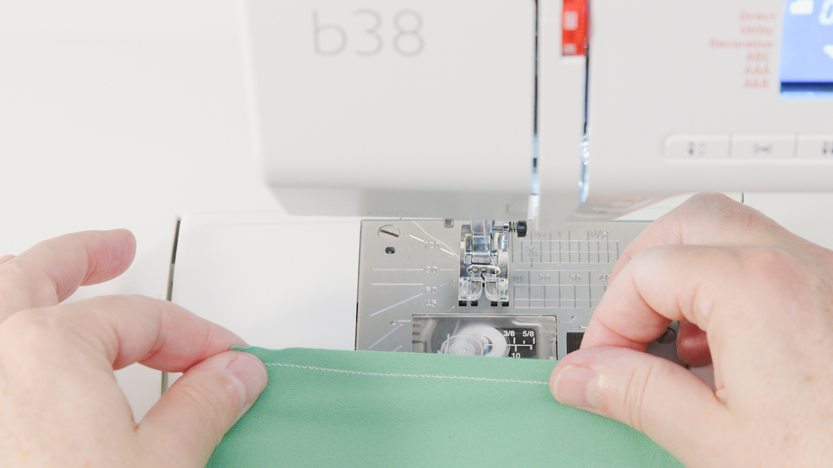 Hands holding green jersey knit fabric to show off the perfect seam