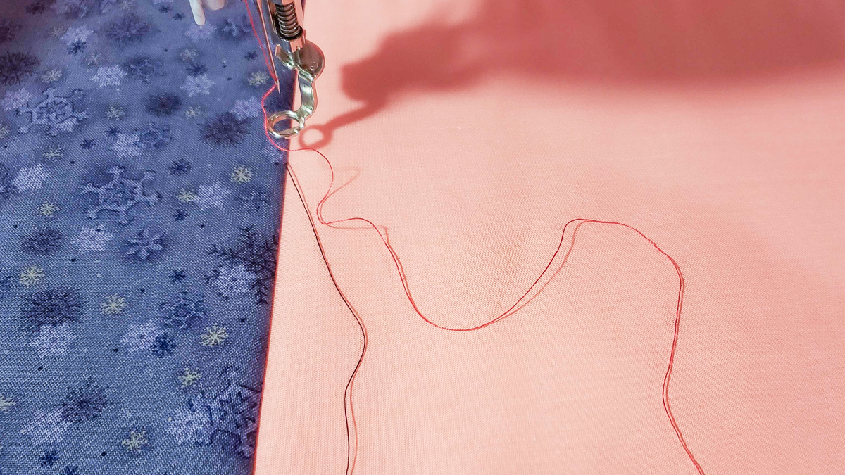 Overhead view of orange and blue/grey fabric, with quilted red thread.