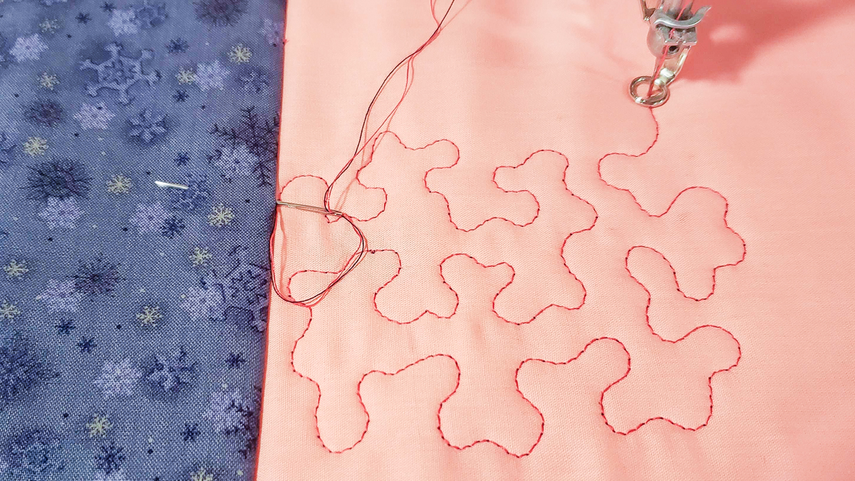 Overhead view of orange and blue/grey fabric, with quilted red thread.