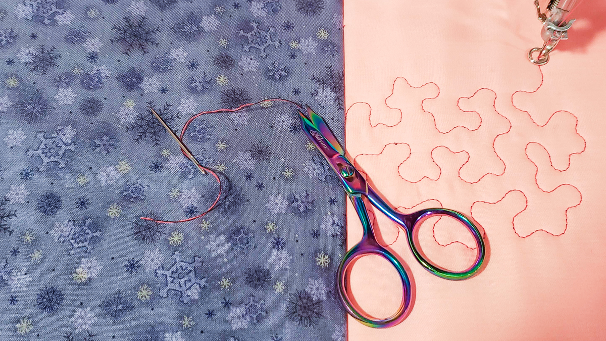 Overhead view of orange and blue/grey fabric, with quilted red thread and scissors
