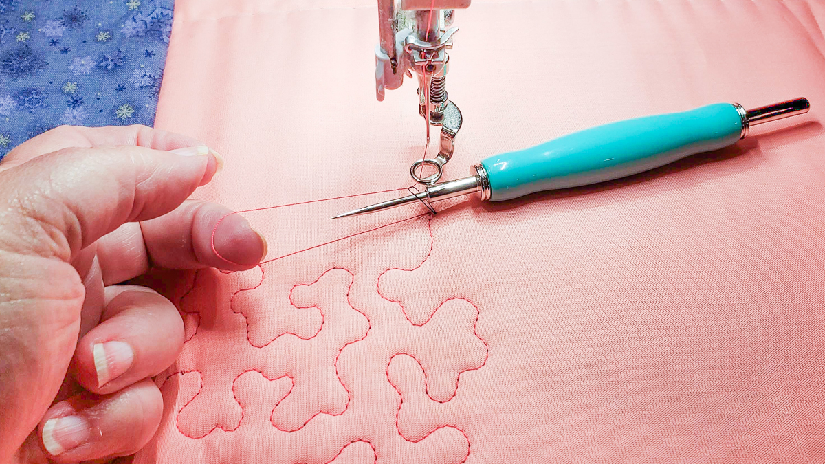 Overhead view of orange and blue/grey fabric, with quilted red thread and a stilleto