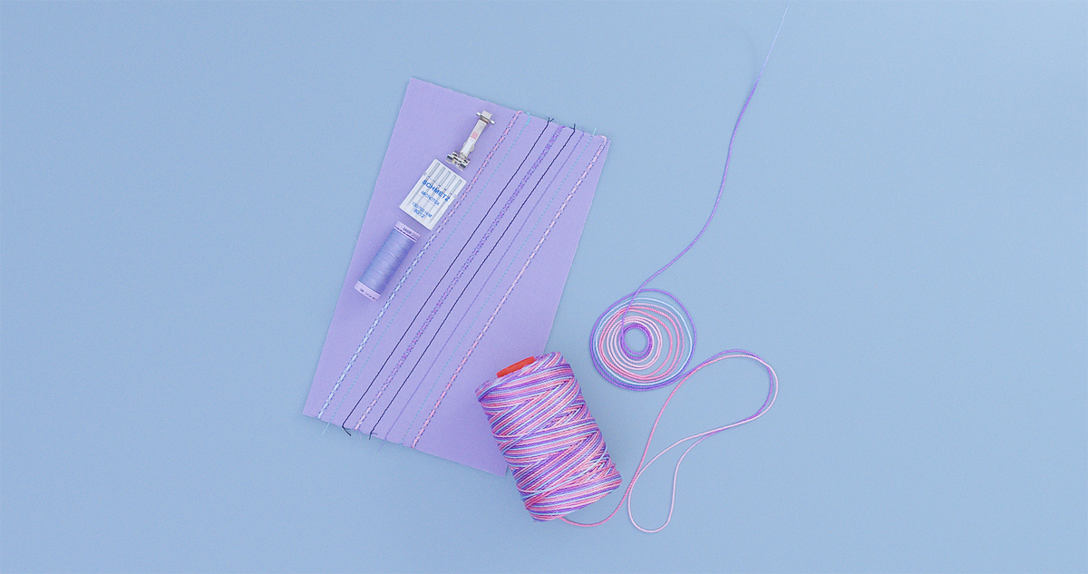 Purple fabric sample with straight stitching lines alongside spools of variegated nylon cording for couching technique