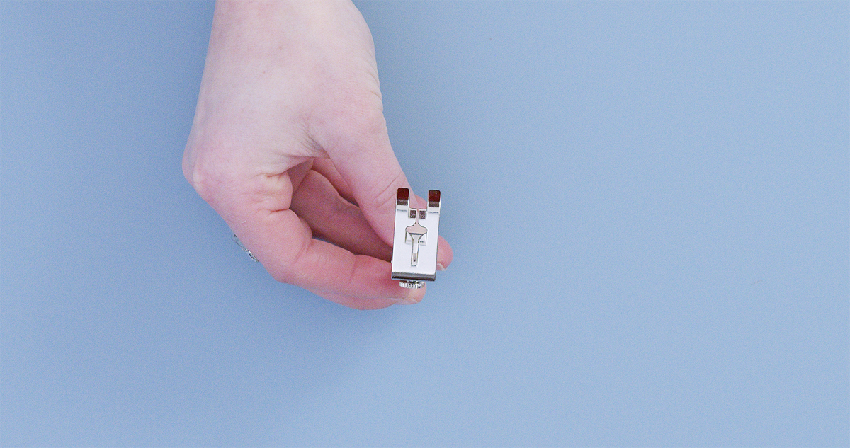 Hand holding the underside of Cordonnet Foot #11, displaying the 2 mm center groove designed for thick thread guidance