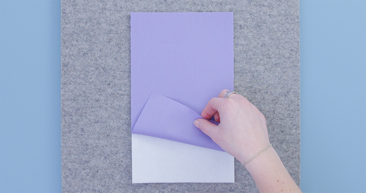 Hand applying fusible stabilizer to purple fabric on a gray pressing mat