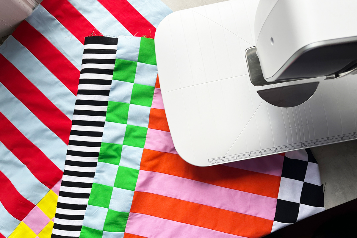 A top-down view of the Checks Mix quilt draped on a table in Jaclyn's sewing studio. The B 735 sewing machine peeks in from the right side of frame.