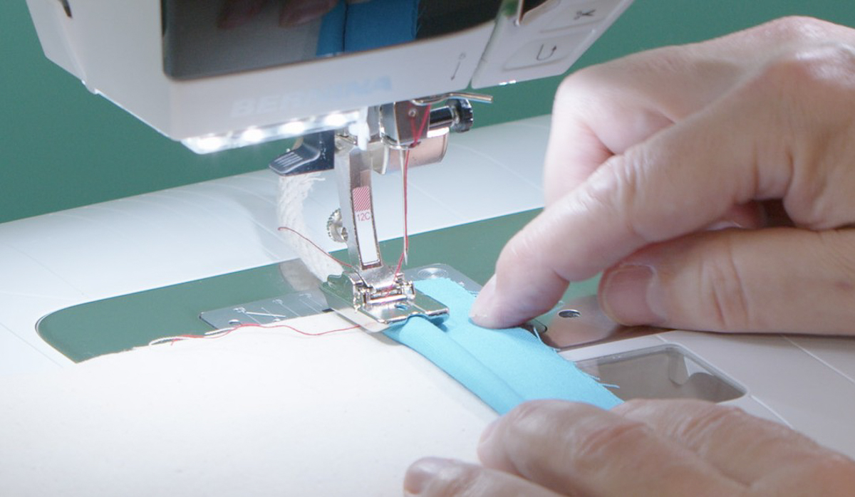 sewing blue fabric-wrapped cording to cream muslin fabric