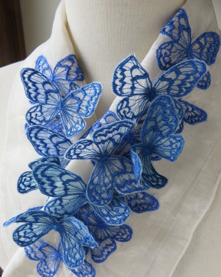 Blue freestanding embroidered butterflies arranged in a dimensional cluster on sheer white fabric draped over a dress form.