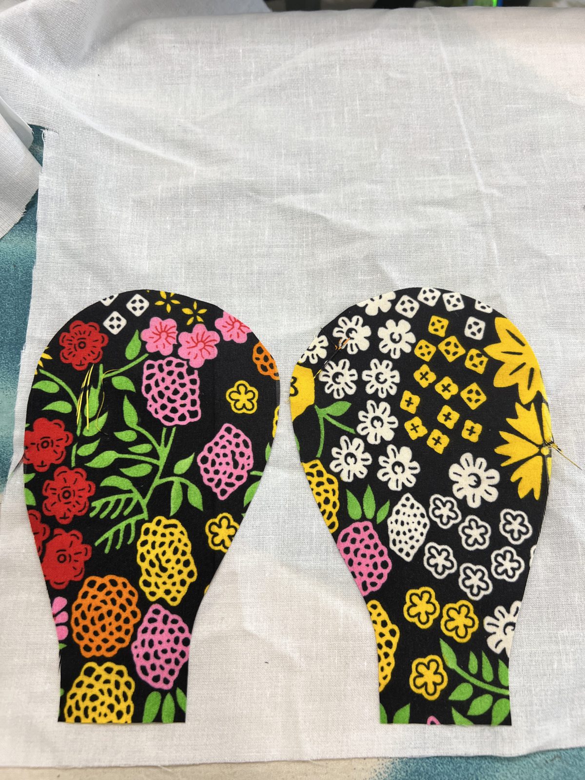 Two large rounded flower petals cut from colorful floral Ankara fabric featuring red, pink, yellow, orange, white, and green botanical motifs on a black background.
