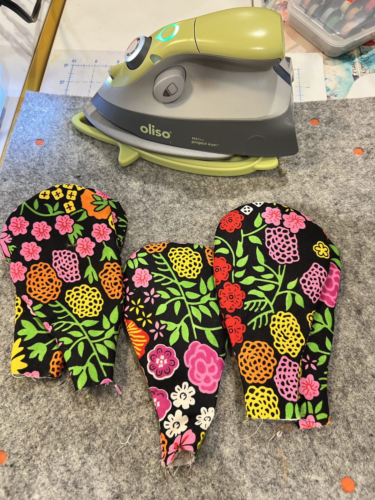 Colorful floral Ankara fabric petals freshly pressed and arranged on a gray pressing mat beneath an iron, ready to be shaped and assembled into a fabric flower.