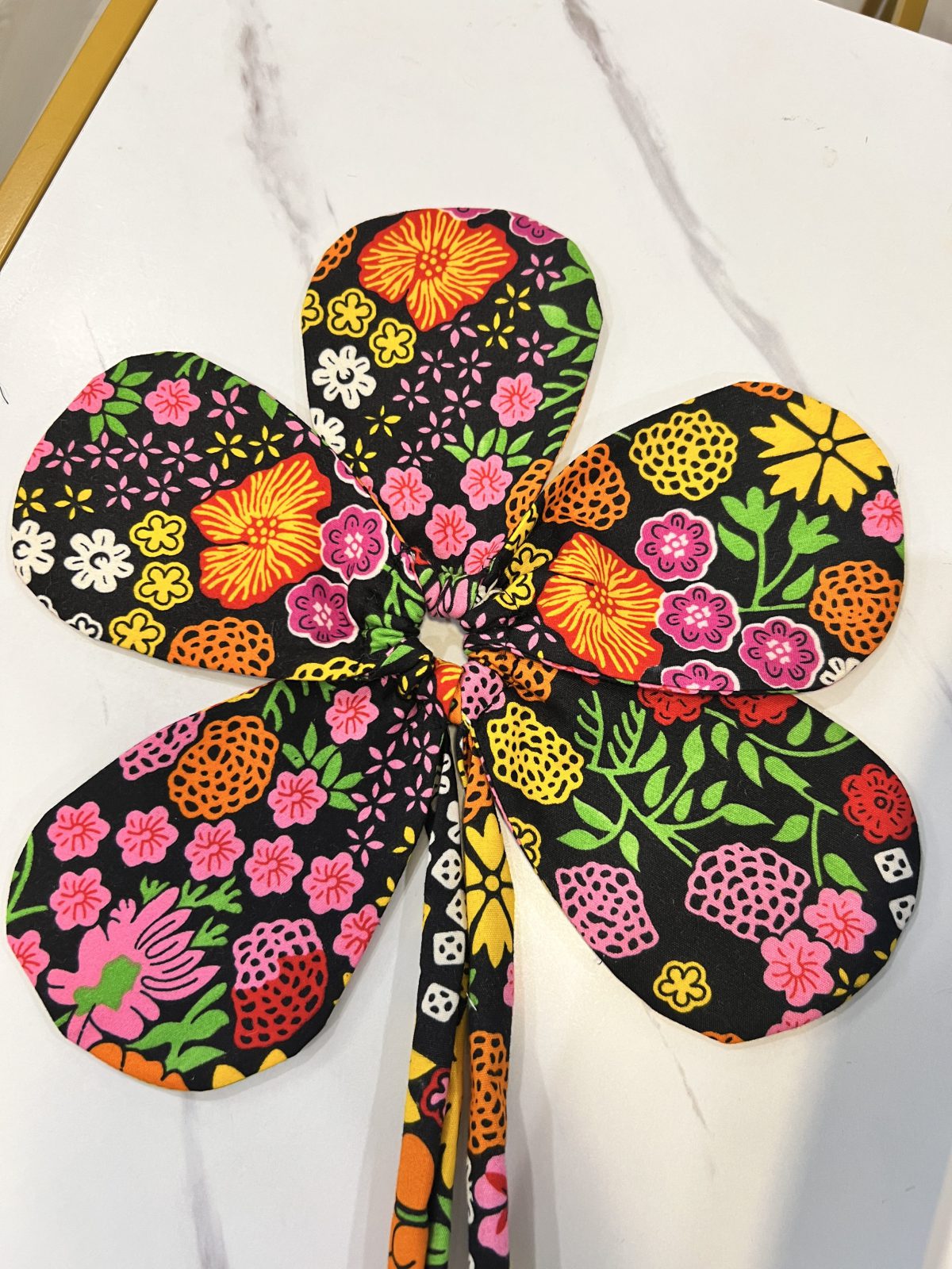 Five large colorful floral Ankara fabric petals arranged and gathered together in a flower shape, with a coordinating fabric tie extending from the center.
