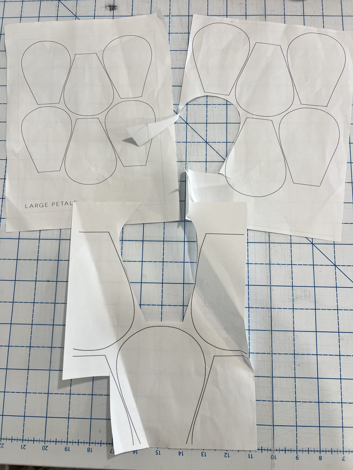 Paper sewing pattern pieces for large flower petals laid out and partially cut on a gridded cutting mat