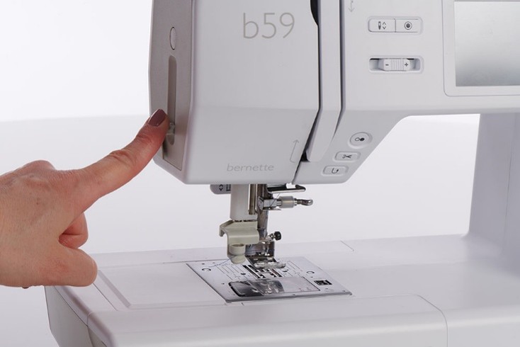 A hand engaging a lever to automatically thread a sewing machine needle