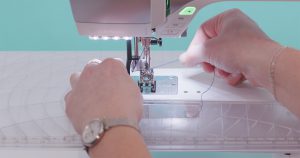 A compact sewing machine with embroidery module attached and smart phone, displaying embroidery design information, positioned on top