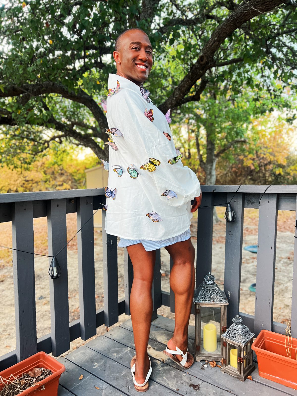 Smiling Black man modeling the back and side of a handmade oversized white linen shirt decorated with colorful three-dimensional embroidered butterflies.
