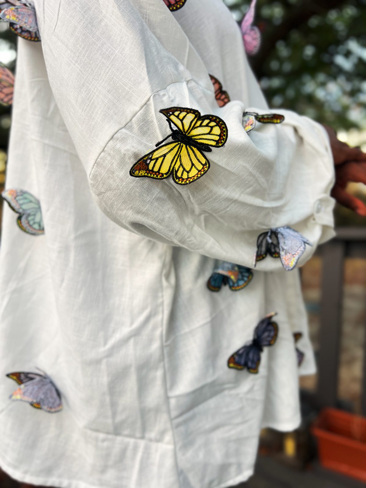 Close-up of colorful freestanding embroidered butterflies attached to white linen fabric, with dimensional wings in blue, green, yellow, pink, purple, and black.