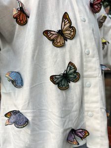 Close-up of colorful freestanding embroidered butterflies attached to white linen fabric, with dimensional wings in blue, green, yellow, pink, purple, and black.