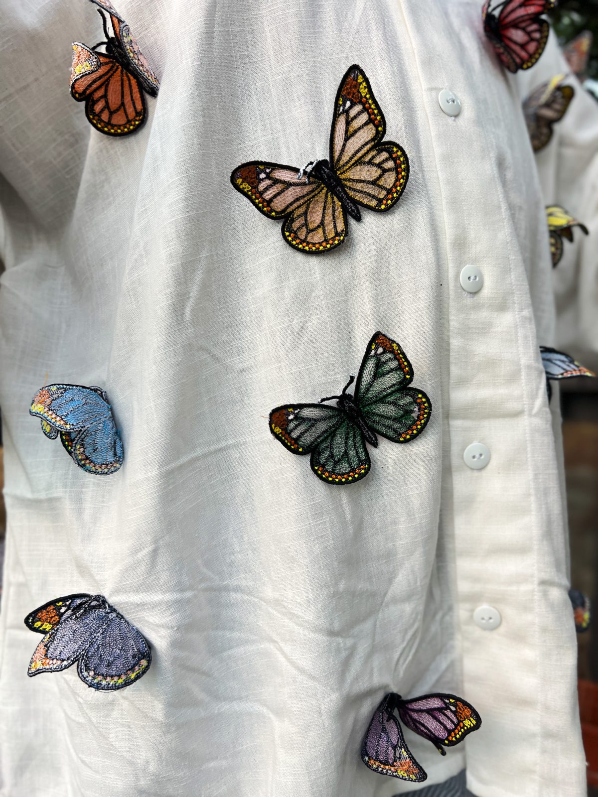 Close-up of colorful freestanding embroidered butterflies attached to white linen fabric, with dimensional wings in blue, green, yellow, pink, purple, and black.