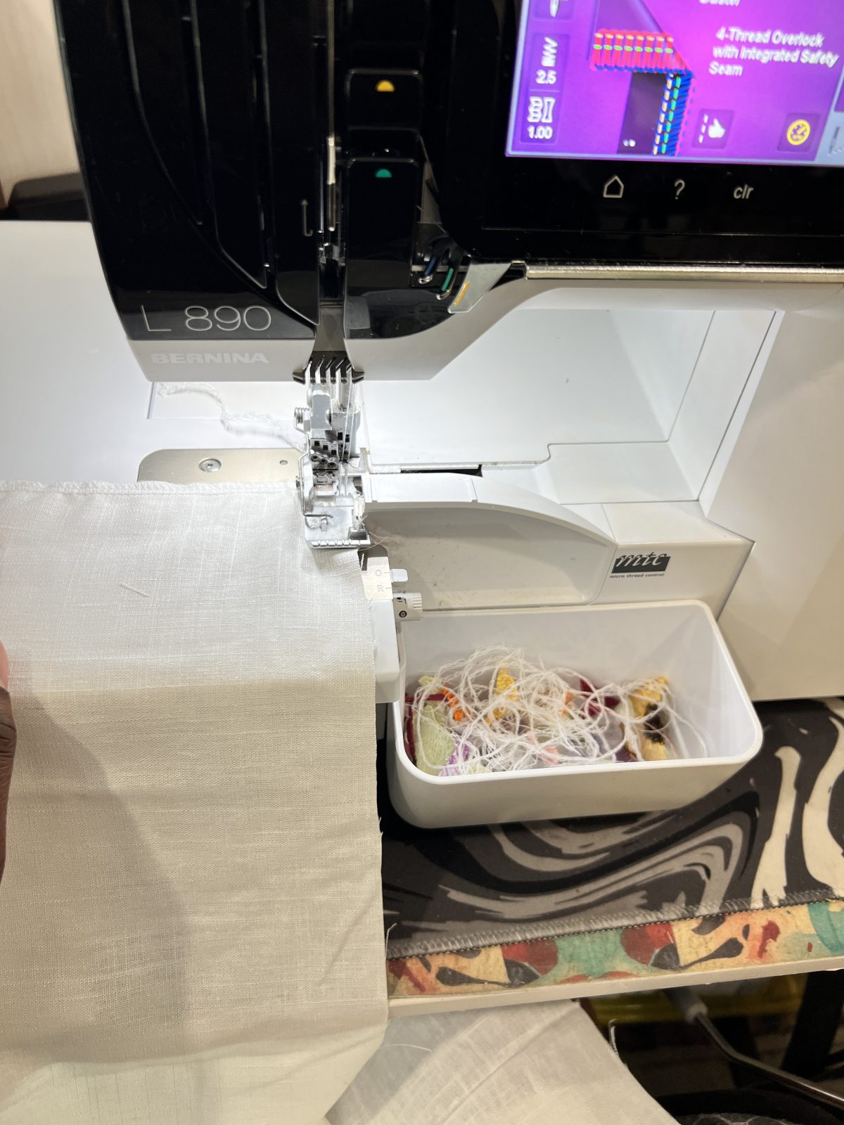White linen fabric being finished on a BERNINA L 890 overlocker, showing the serging process along the raw fabric edge.