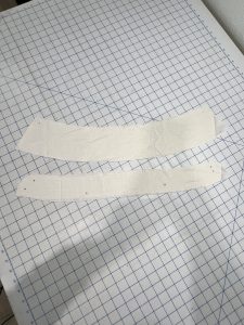 Two curved white linen collar pieces pinned and prepared for sewing on a gridded cutting mat.