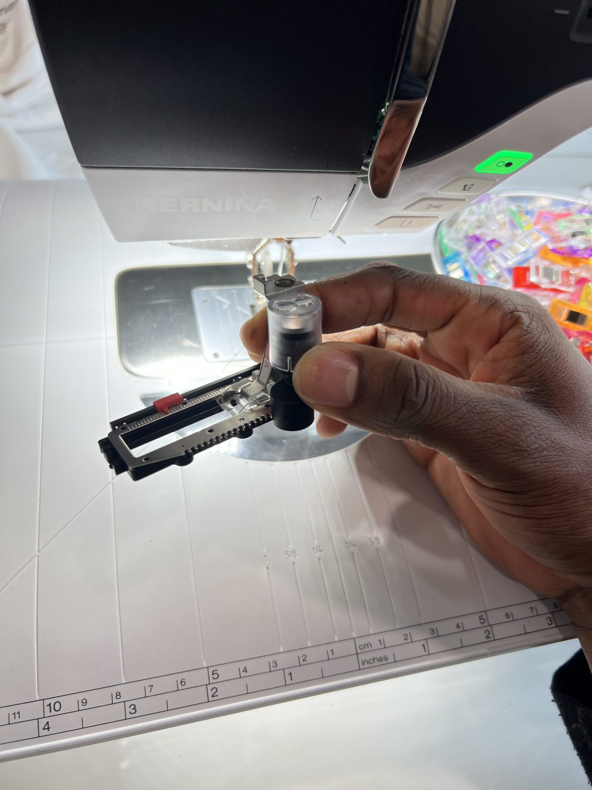 Close-up of a BERNINA sewing machine buttonhole foot being held in front of the machine, ready to create buttonholes for a handmade shirt.