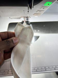 Close-up of two neatly stitched buttonholes on white linen fabric in front of a BERNINA sewing machine.