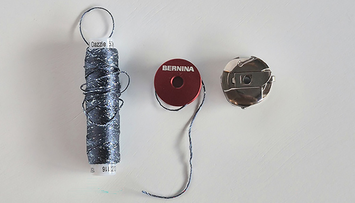 Spool of Dazzle 8 weight thread by Wonderfil, with bobbin and bobbin case.